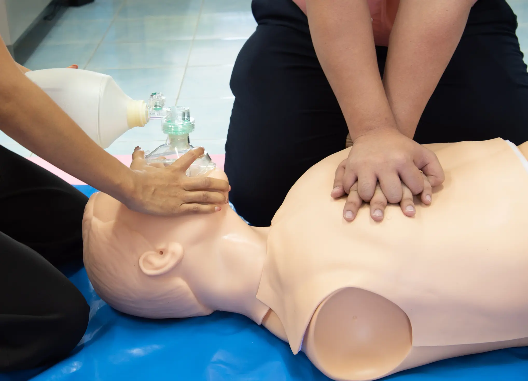 Close-up of two trainees practicing CPR on adult mannikin, one performing chest compressions while another administers rescue breaths using bag valve mask during first aid certification course